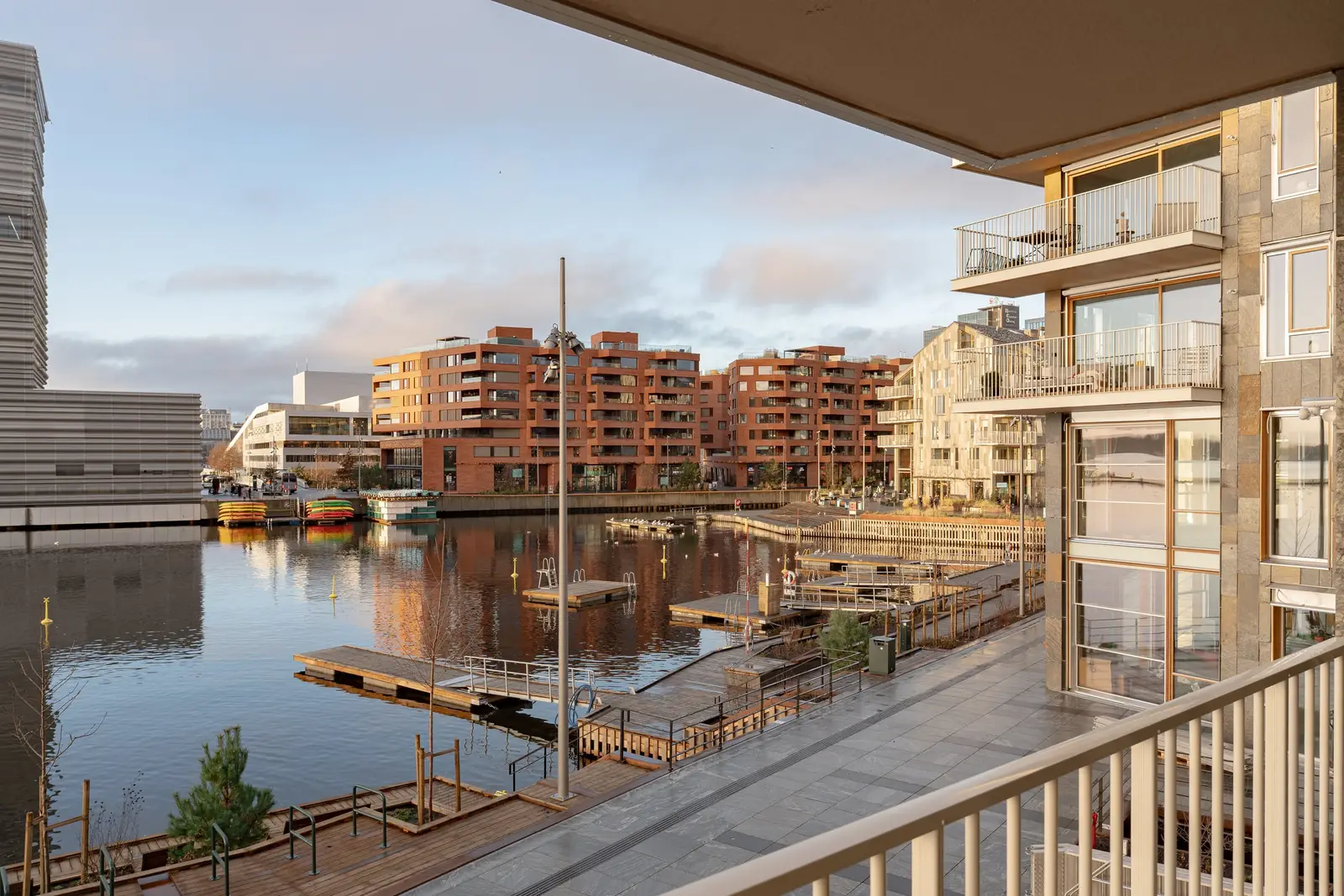 Utsikt fra en balkong over havnebassenget, med bryggene nedenfor og røde teglbygg på motsatt side.