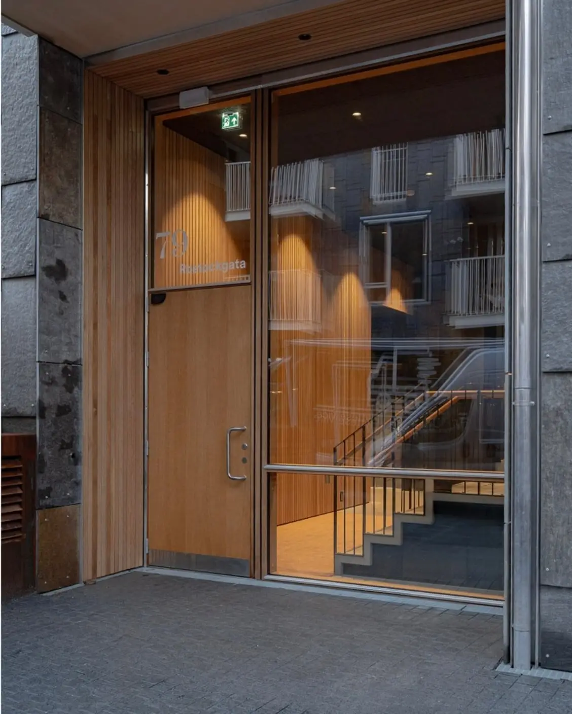 Inngangspartiet i Rostockgata 79, med dør i eik og trappen opp innenfor glassfasaden.