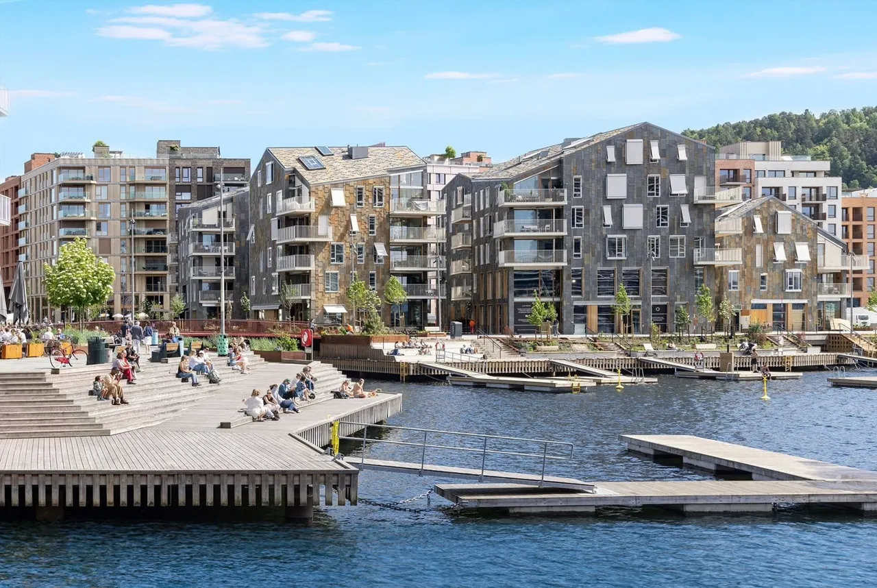 Havnepromenaden foran husene, der folk sitter i sola på bryggetrappene.