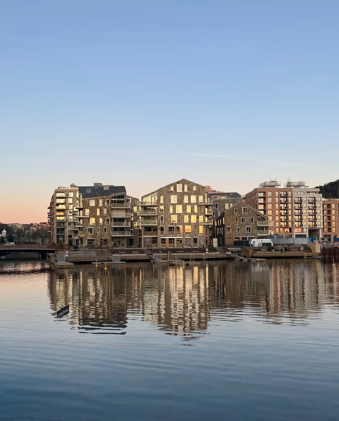 Husene sett fra vannet i solnedgang, med speilinger i fjorden.